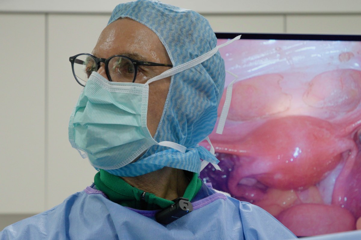 Dr. Camran Nezhat in surgical cap and mask beside a monitor showing the laparoscopic view.