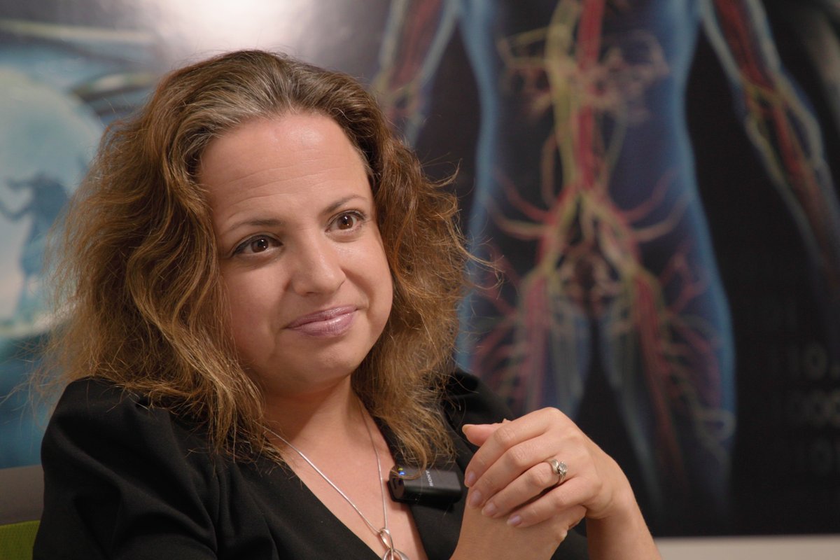 Dr. Marina Sirota seated for an interview in front of a large anatomical illustration.