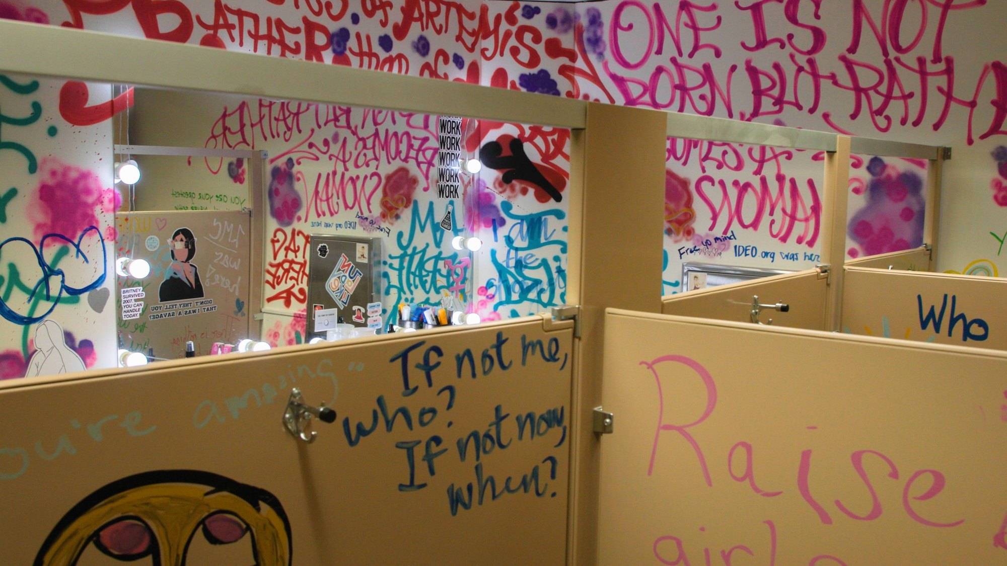A bathroom wall covered in hand-painted slogans, including "If not me, who? If not now, when?"