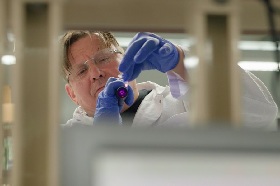 A scientist holding a sample vial up to the light in a laboratory.