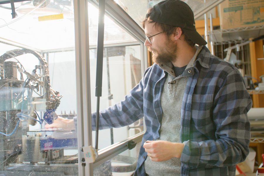 A researcher working at a bioprinting rig behind an acrylic enclosure.