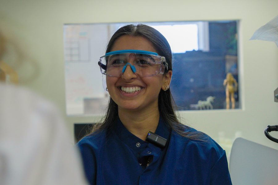 A scientist in blue safety goggles smiling broadly in a laboratory.