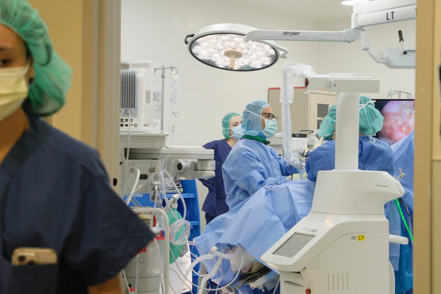 A nurse in a surgical cap in the foreground, the operating room and its team beyond.