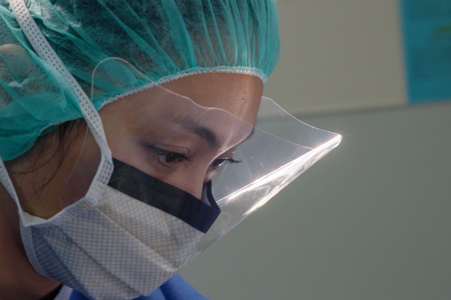 A gowned and masked member of the surgical team in profile, face shield catching the light.